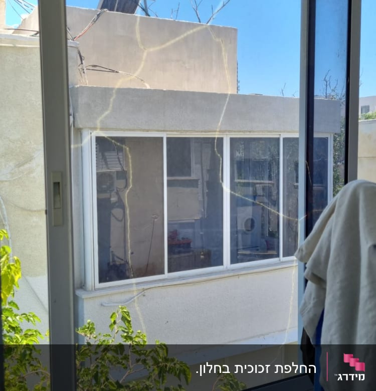 חלון זכוכית עם סדקים גדולים וענפים ברקע